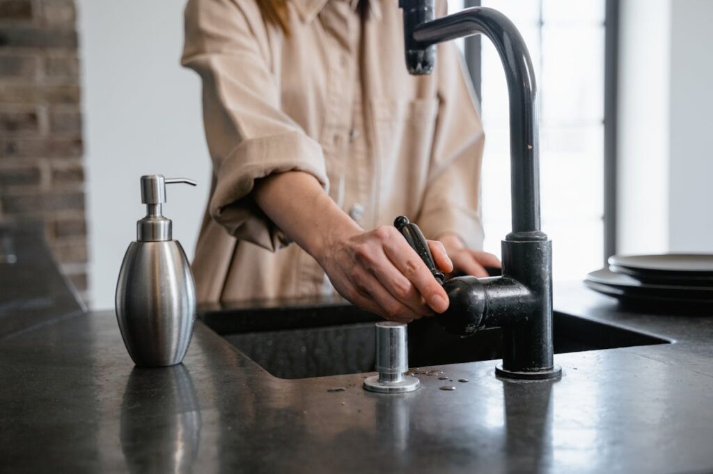 Close-up of a person washing hands at a black kitchen sink with a soap dispenser.