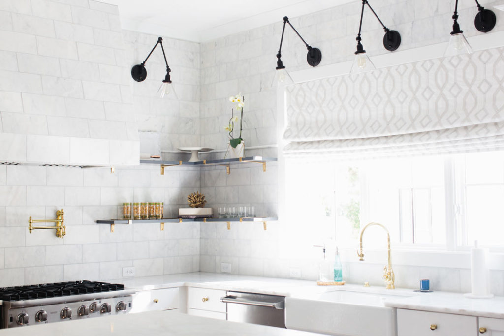 White kitchen with brass Waterstone faucet and black sconces for lighting.